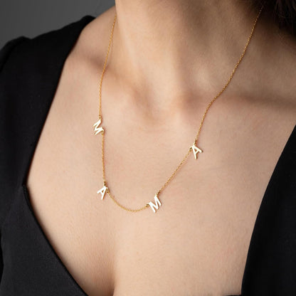 Gold necklace with letter pendants on a person wearing a black top.