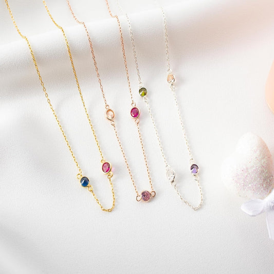 Three delicate necklaces with colorful gemstones on a light background