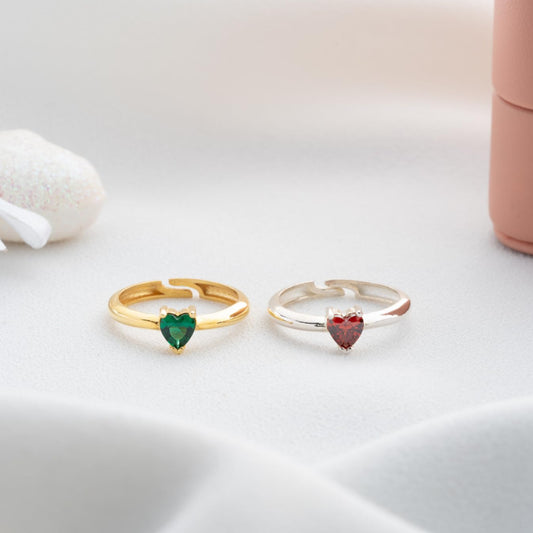 Two heart-shaped gemstone rings, one gold and one silver, on a light background.