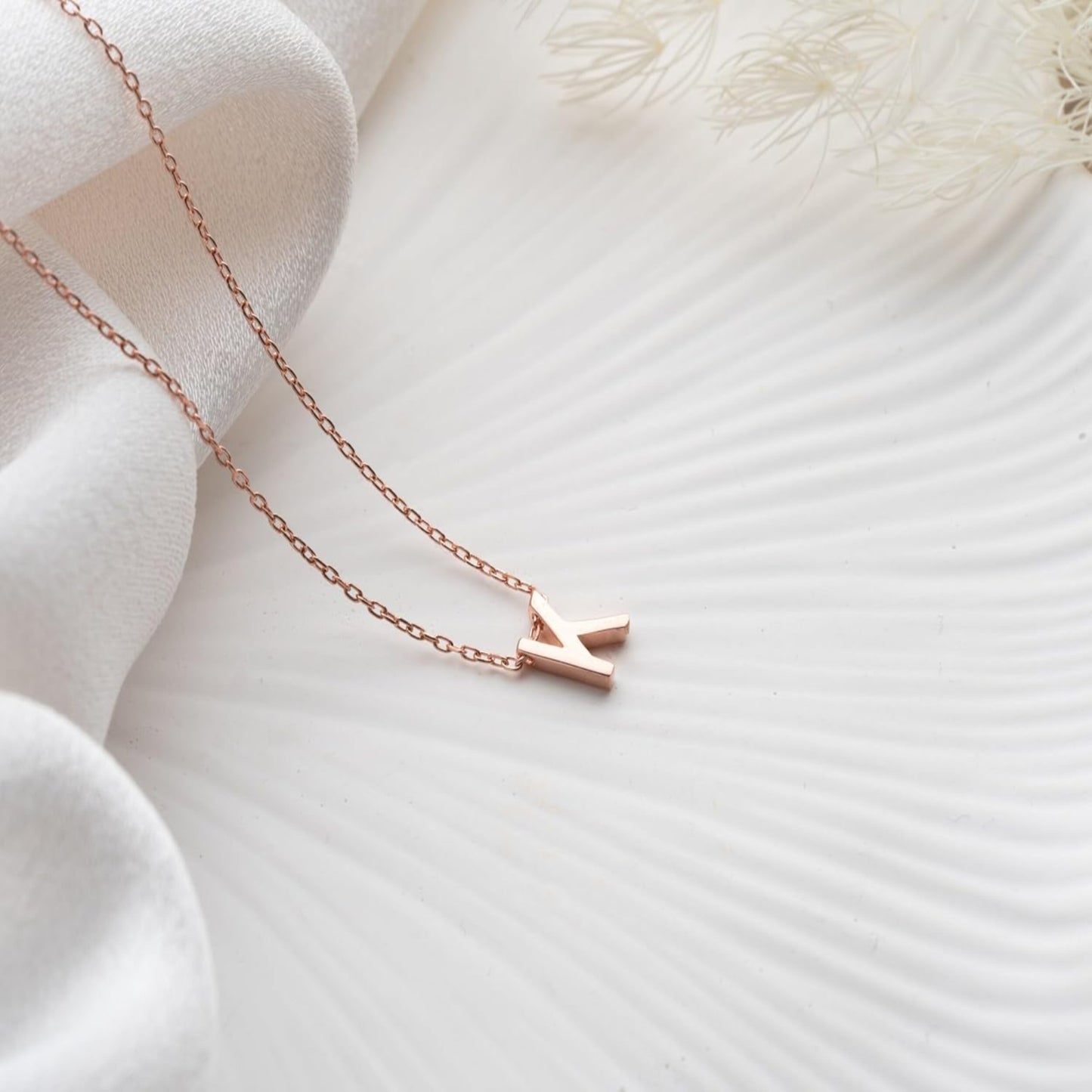 Rose gold necklace with a small pendant on a soft white fabric background