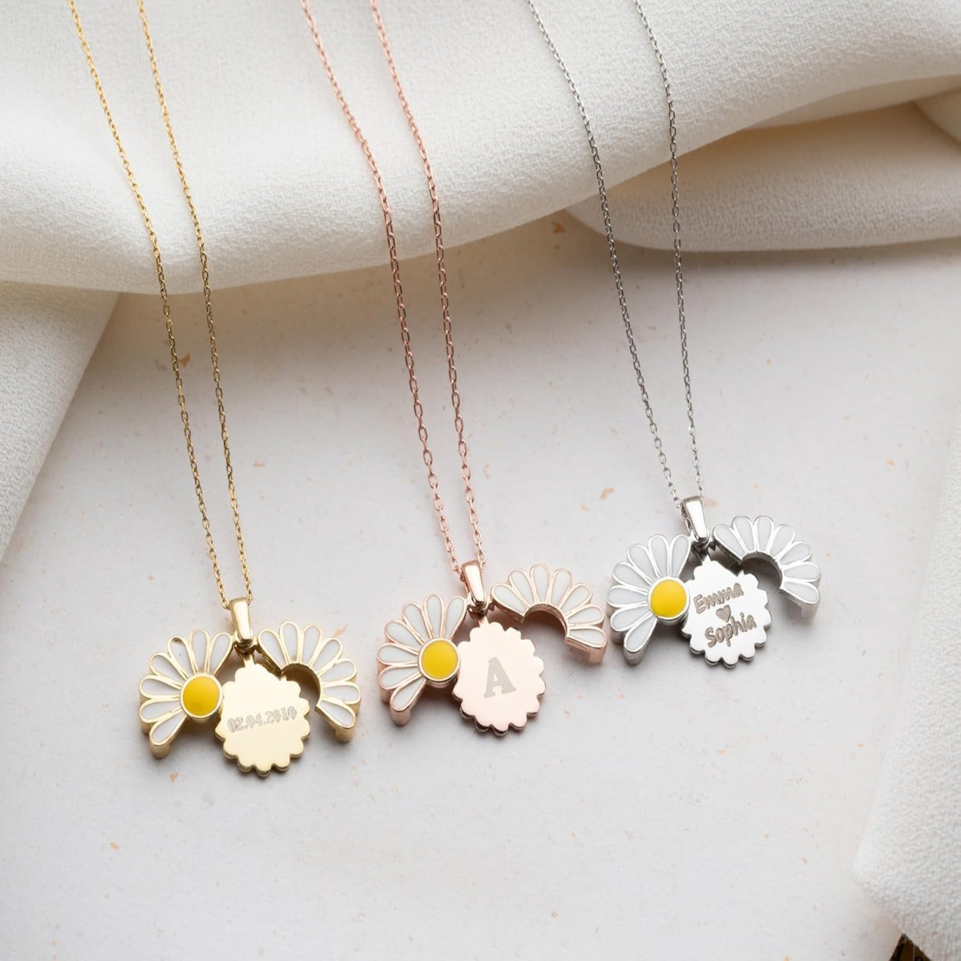 Three floral necklaces with engraved names on a light fabric background