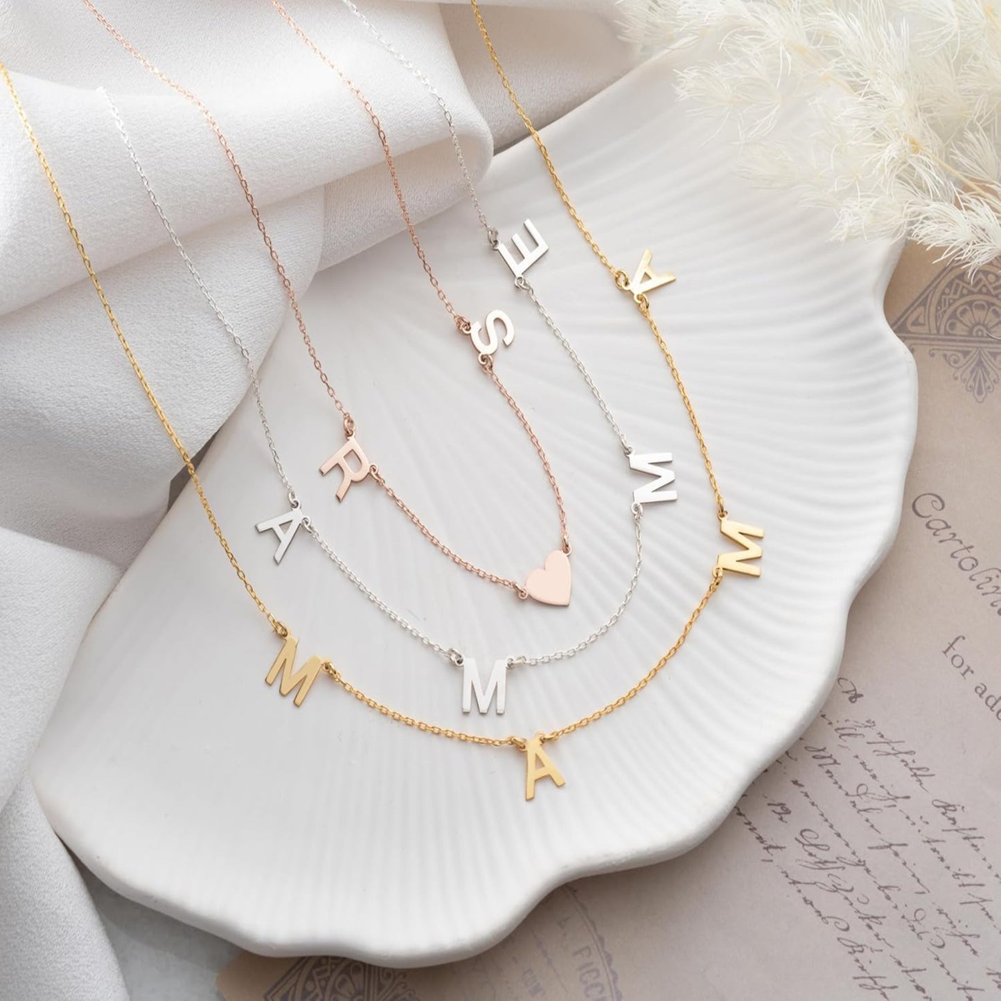 Three gold necklaces with letter pendants on a white dish.