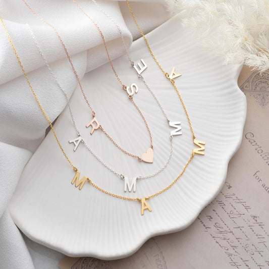 Three gold necklaces with letter pendants on a white dish.