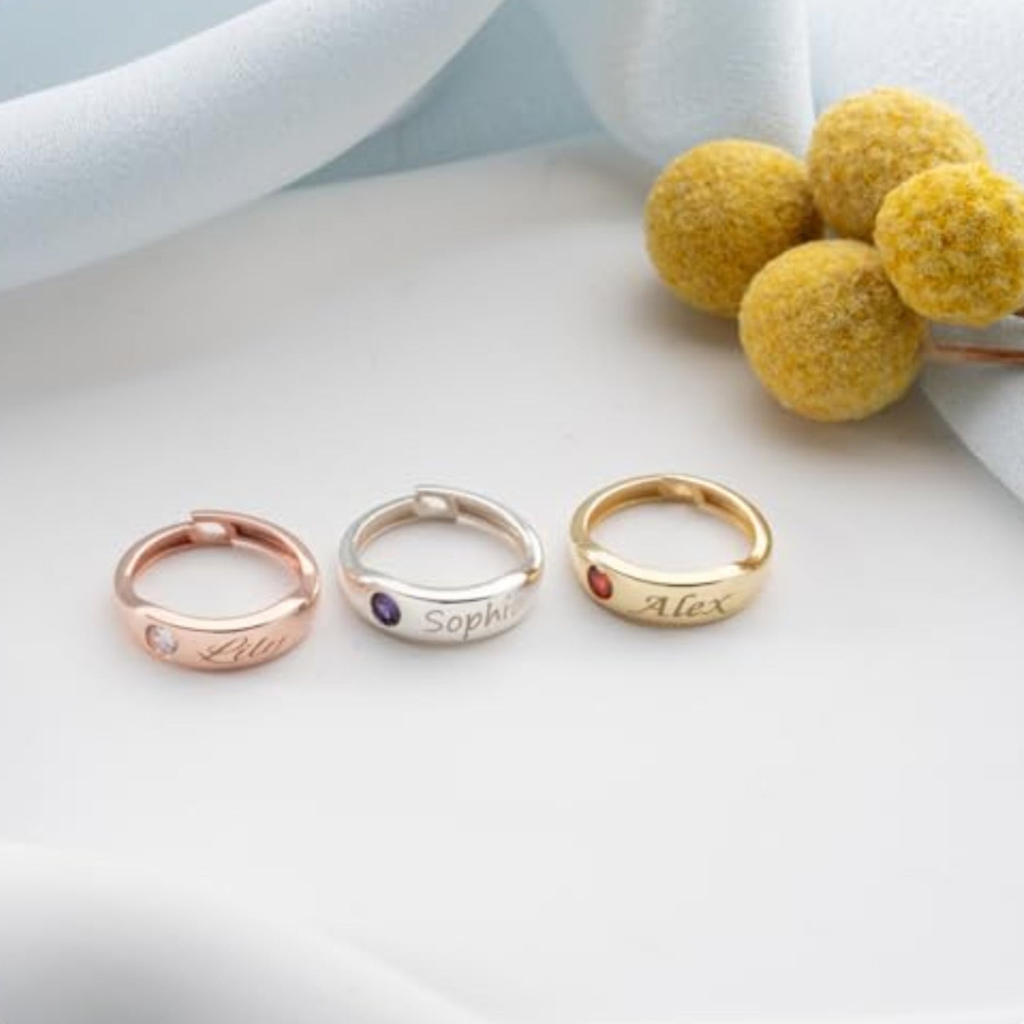 Three personalized rings with names engraved on a light background with decorative elements.