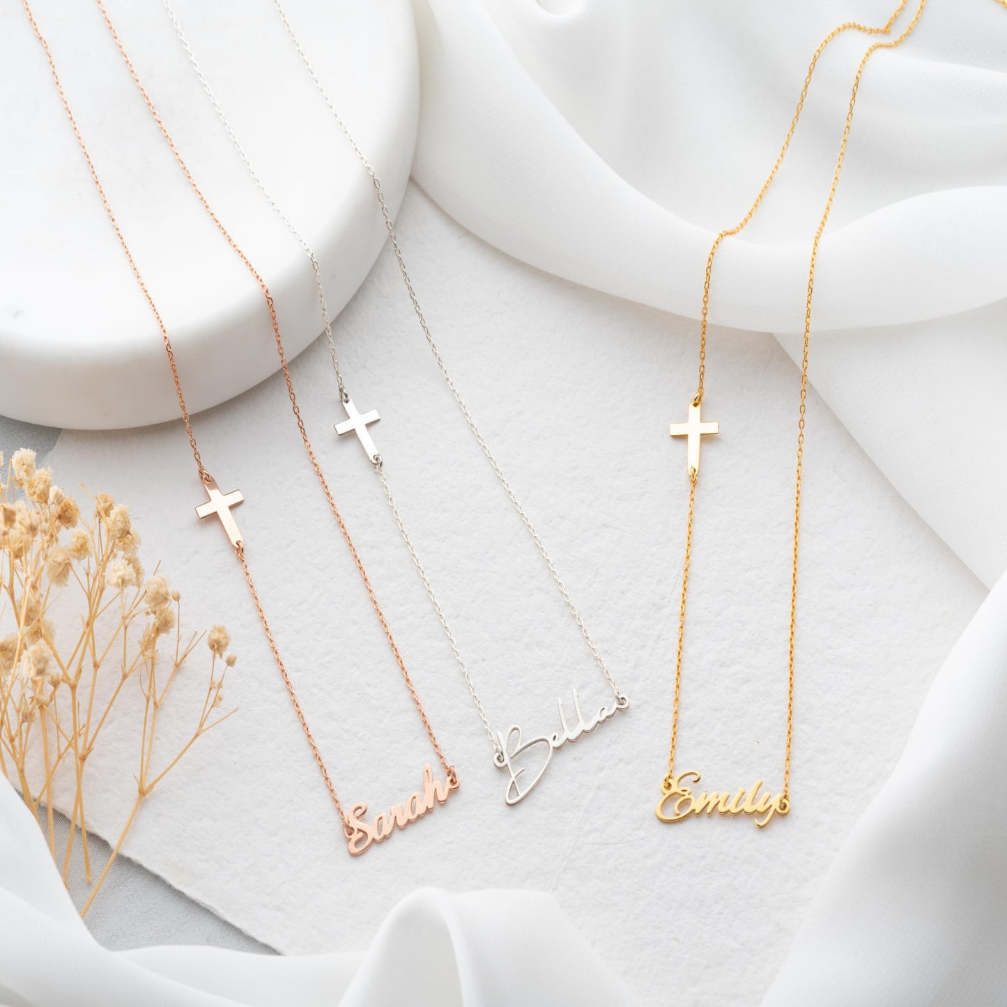 Three gold necklaces with engraved names on a white fabric background