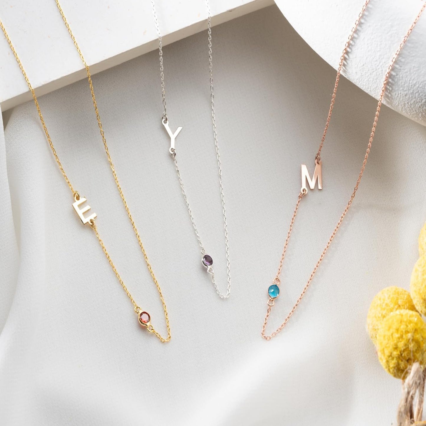 Three necklaces with letter pendants on a white surface.