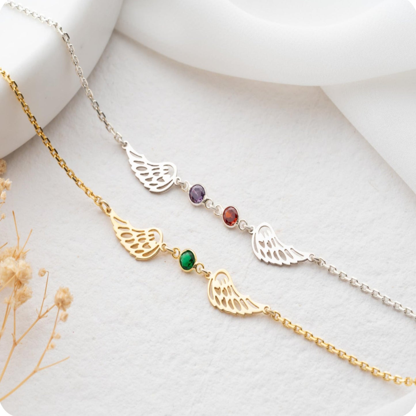 Two angel wing necklaces with gemstones on a white surface.