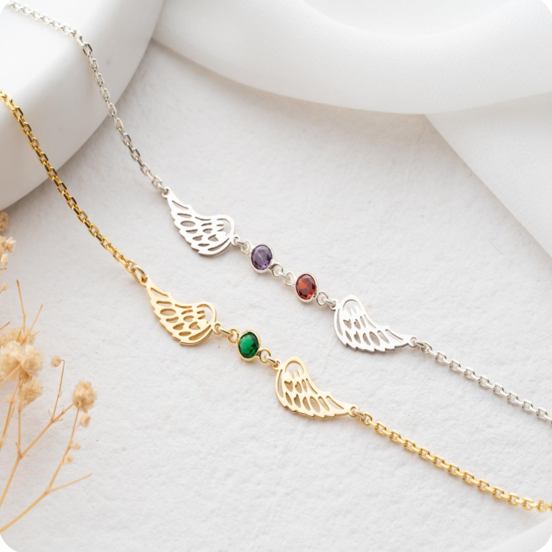 Two angel wing necklaces with gemstones on a white surface.