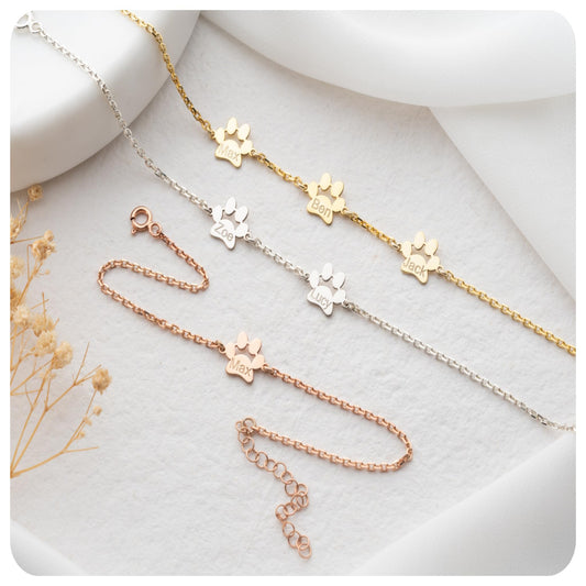 Three gold, silver, and rose gold necklaces with paw print designs on a light background.